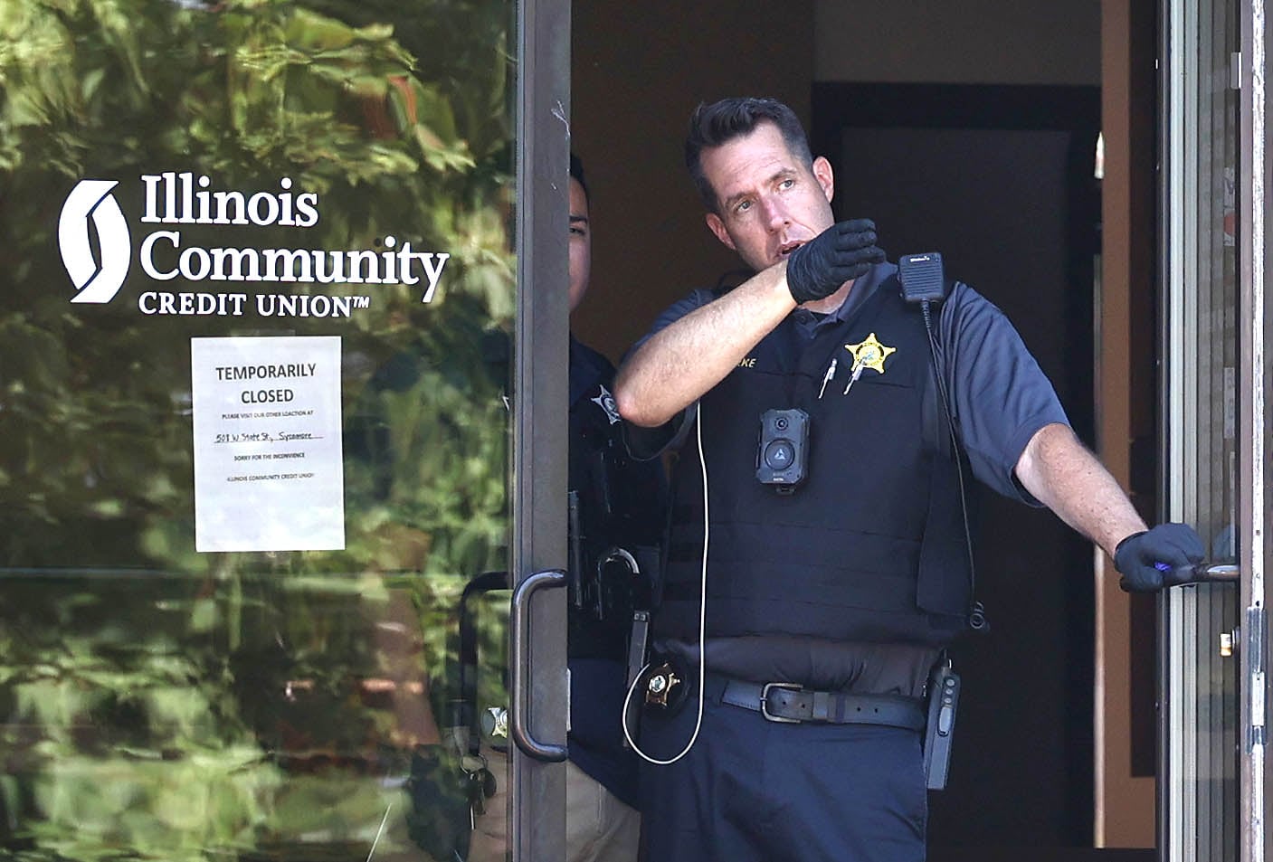 DeKalb police officers look out the door of the Illinois Community Credit Union Wednesday, July 31, 2024, as they investigate a morning bank robbery in the facility at 1500 Barber Greene Road in DeKalb.
