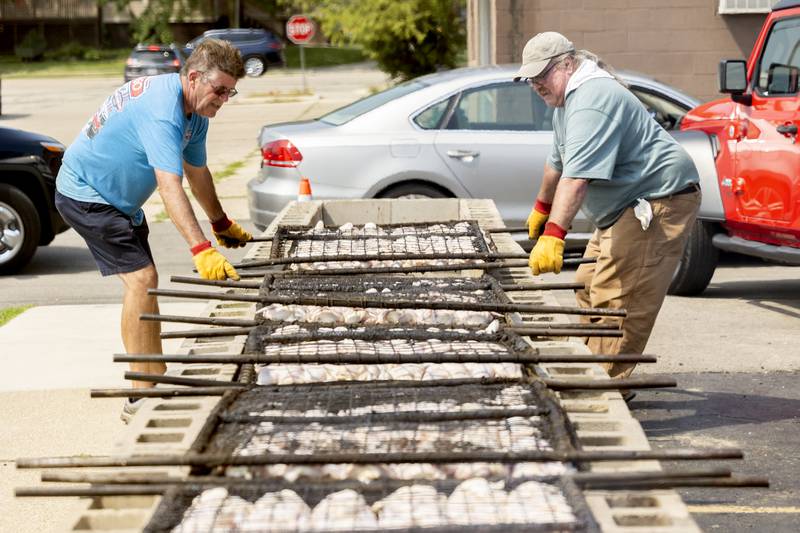 Terry Hammett (left) and Tim "Snuffy" Bittner place a rack of chickens over charcoal Monday, Aug. 5, 2024, for the American Legion barbecue lunch.
