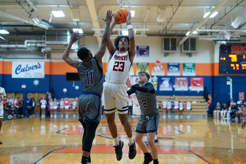 Oswego’s Dasean Patton (23) shoots the ball in the post against Oswego East's Reginald McWaine (11) and Lukas Adolfs (12) during a basketball game at Oswego High School on Tuesday, February 18, 2025.