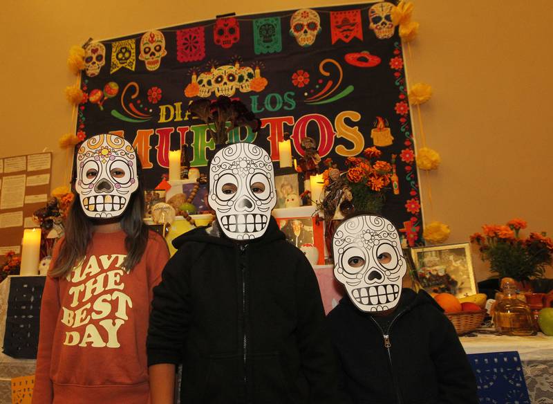 Sophia Leon, 10, stands next to her cousins, Jeronimo Medrano, 8, and his brother, Alan, 5, all of Round Lake Park as they wear masks while standing next to an altar honoring loved ones who have passed away during the Day of the Dead Celebration at the Round Lake Beach Cultural & Civic Center.