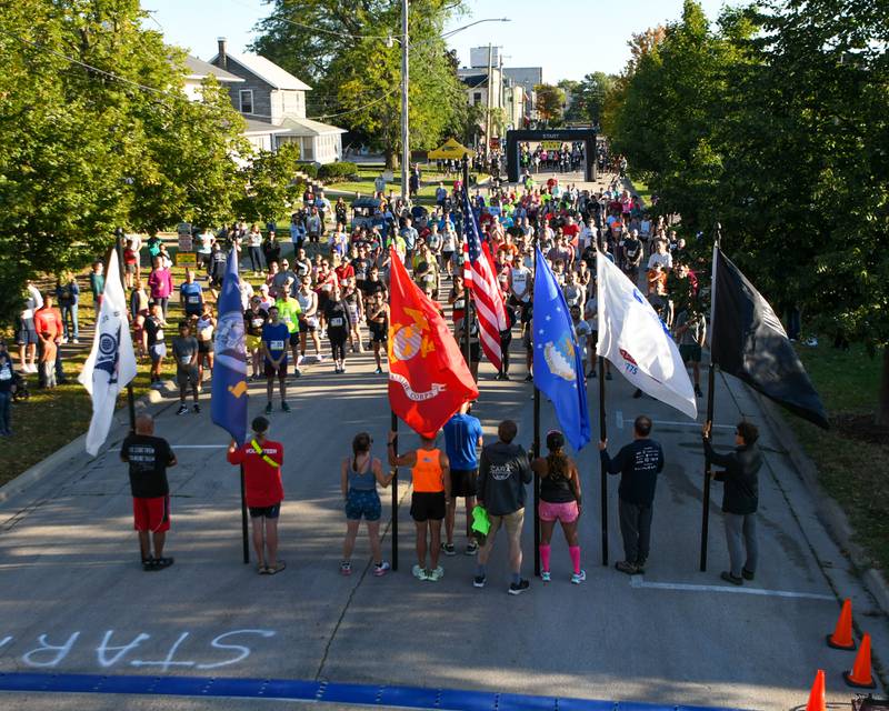 Military members run in the DeKalb Corn Classic 5K/10K races on Sunday, Sept. 29, 2024, while holding their respective branch flags as the national anthem is sung before the start of the race in downtown DeKalb.