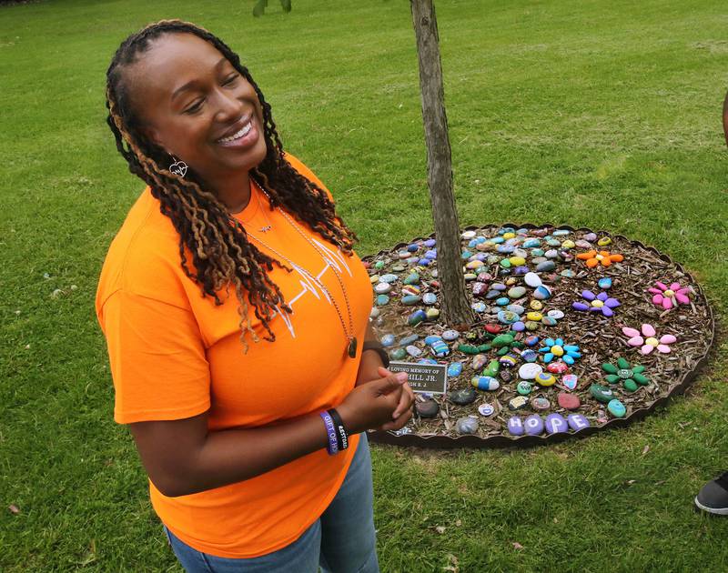 Andrea Elion, mother of Ezra Hill Jr. smiles as she talks Monday, May 12, 2025, about him next to a tree and rock garden at Tyler Elementary School, where he attended, that is dedicated to his memory. Hill was murdered in 2019 in Harvey, and the Fifth Annual Ezra Hill Jr. Memorial Rock Painting event will be held on June 7 at the school in DeKalb.