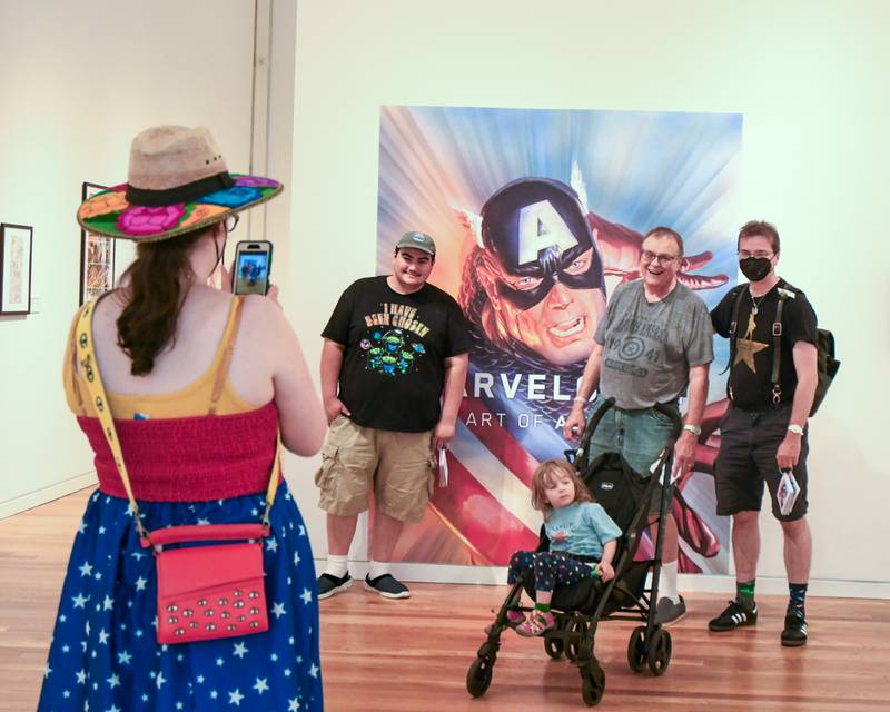 Elisa Shoenberger of Chicago takes a photo of her husband Montgomery Priz and Daughter Alice Priz-Shoenberger, 2 years old, Ed Priz of Hillside and Noah Steciak of Hillside during the Marvelcity: The Art of Alex Ross exhibit on Saturday June 24, 2023, held at the Elmhurst Museum.