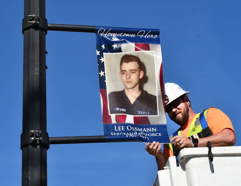 Oregon Public Works employee Josh Pickering adjusts the first veteran banner featuring Lee Ossmann on a city light pole in downtown Oregon on Thursday, April 23, 2026. Ossmann served in the Air Force during the Vietnam War and is an active member of Oregon VFW Post #8739.