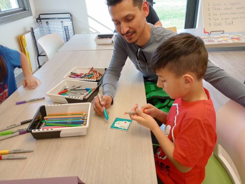 Pingree Grove resident Edgar Garcia sat in the art room with his son Bash, 5, at the reopening of Fox Valley Hands of Hope in Geneva Friday, April 28, 2023, coloring a tile that will be used in a mosaic. The art room is new, the result of a major renovation, offering a space where participants can use art to help process grief.