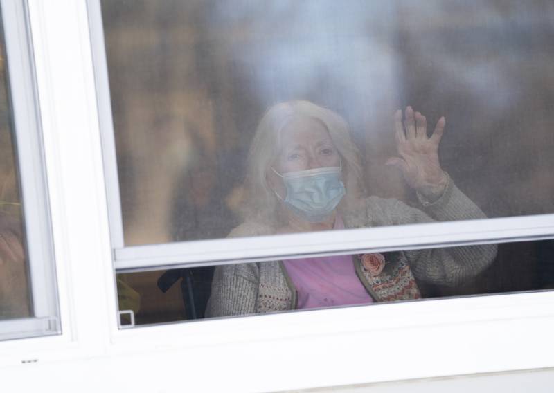Virginia Jones waves out the window during a presentation by the Combined Veterans Honor Guard outside the building during a 100th birthday celebration Friday, Jan. 22, 2021, for her. Jones, a Marine Corps veteran, currently resides at White Oaks at McHenry Nursing and Memory Care in McHenry.