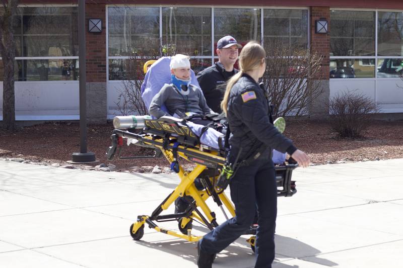 Paramedics taking a student actor to an ambulance outside Joliet West High School on Tuesday, March 25, 2025, as part of a staged emergency drill simulating the aftermath of a gas explosion.