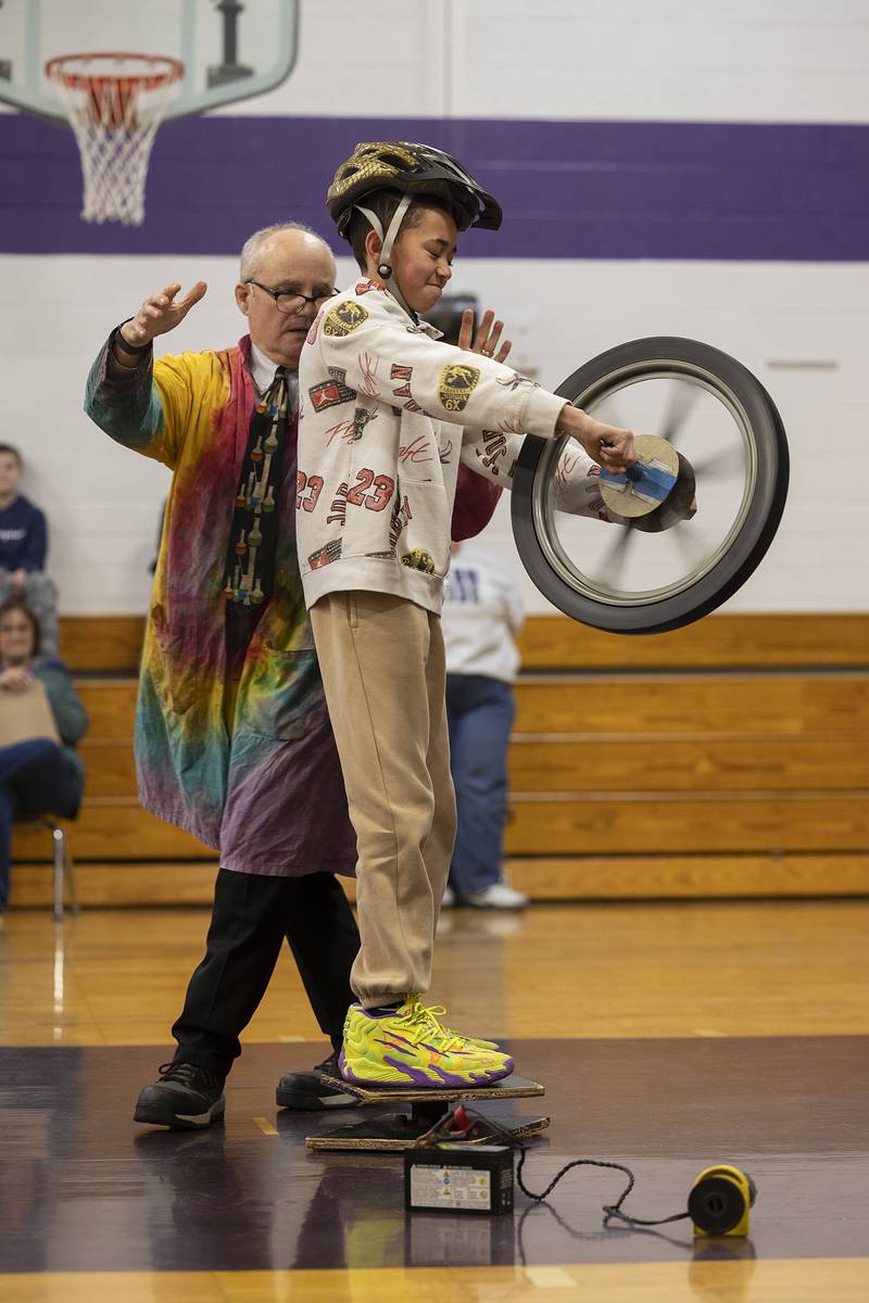 Madison School student Ace Hosford holds on as the force of a spinning wheel moves him in a circle during an experiment by Steve Belliveau Friday, March 7, 2025.