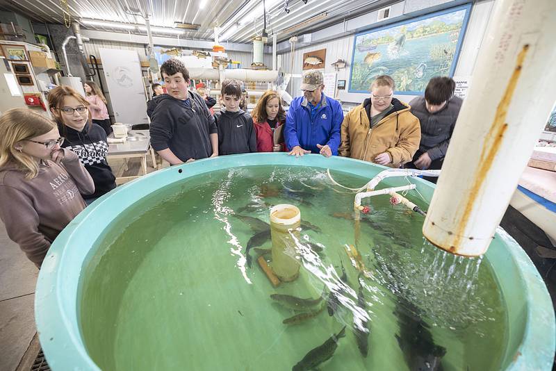 Bob Bradbury (middle in blue) talks to students on a field trip to the Lake Carroll Fish Hatchery Wednesday, April 20, 2023 about the process of growing walleye from eggs during. Volunteers held a week long open house with local school groups coming in to learn the process.