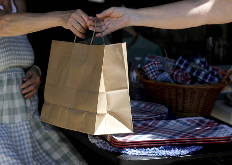 A woman is handed a bag Friday, July 28, 2023, after purchasing an item in Downtown Woodstock. Woodstock in the only McHenry County community to charge a bag fee.