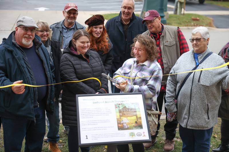 Jaci Kohn, Lockport’s Library Children’s Services Supervisor, cuts a ribbon at the StoryWalk plaque outs the Lockport Library on Saturday, Dec. 10, 2022, in Lockport.