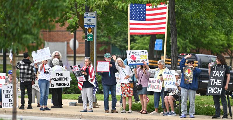 People wave at passing drivers during the "Good Trouble Lives On" protest in Elgin Thursday.