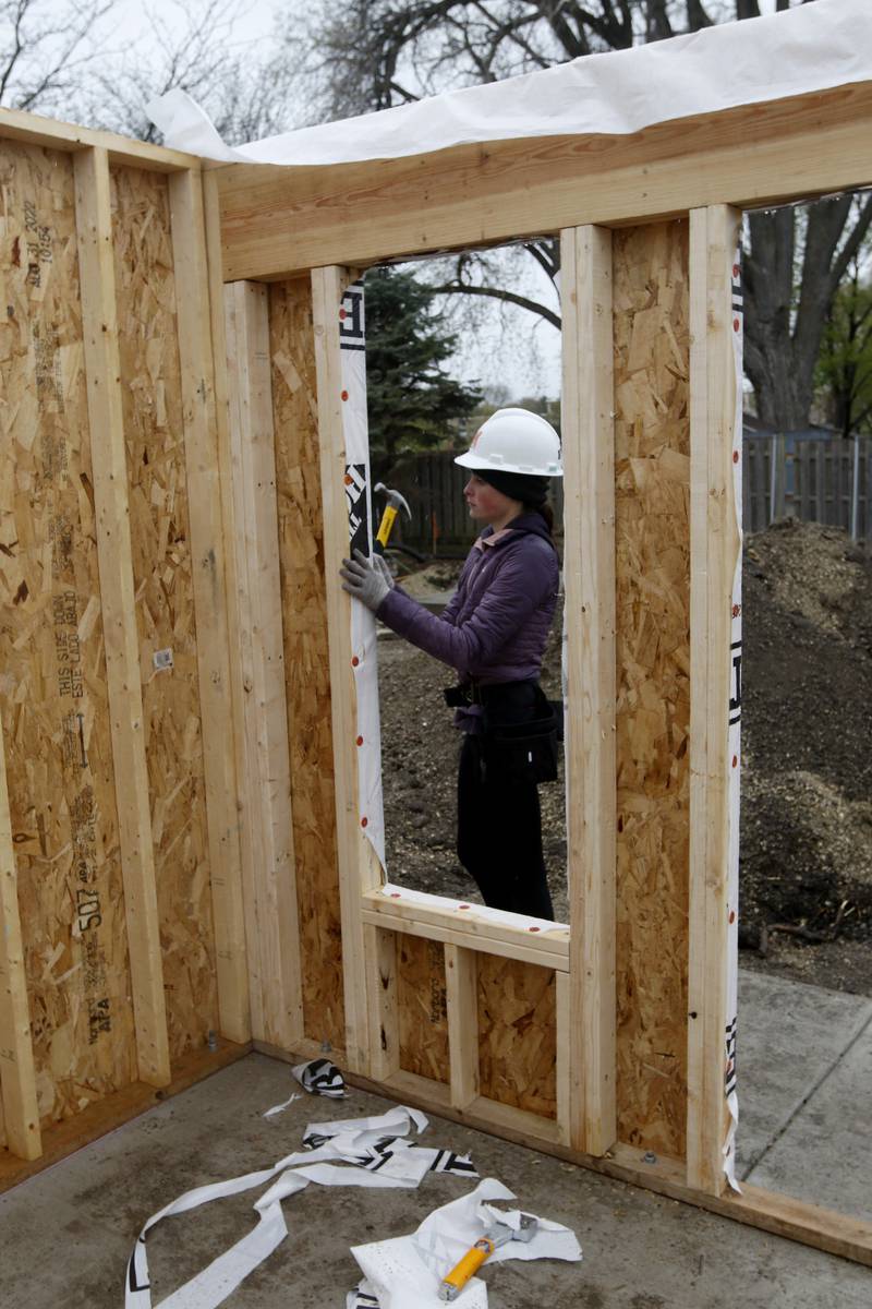 McHenry High School student David May installs weather wrap on a tiny shop being constructed Monday, May 1, 2023, at the new McHenry Riverwalk Shoppes at Miller Point Park in McHenry. McHenry High School students joined volunteers from Habitat for Humanity of McHenry County, McHenry Parks and Recreation Department staff, and contractors to build the shops at the site.