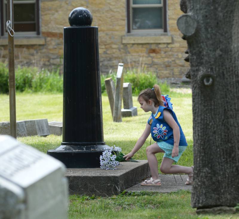 Madelaine Alford, 6, of Oregon, places flowers at a grave during the Oregon VFW's Memorial Day service at Riverside Cemetery in Oregon on Monday, May 26, 2025.