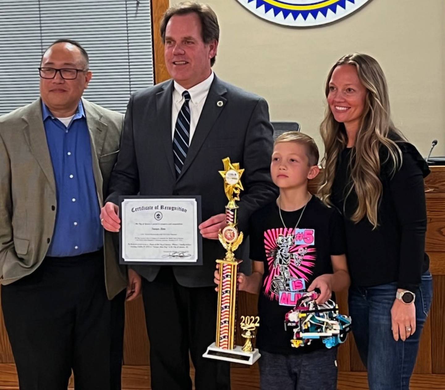 William Wong (left), Geneva Mayor Kevin Burns, Sawyer Rinn, Kristy Rinn at Geneva City Hall Monday where Sawyer was recognized for his first place trophy in the World Robot Olympiad. Wong is Sawyer’s coach in robotics.