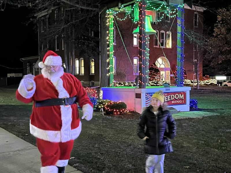 Eden White, 6, of Mt. Morris, walks with Santa past the decorated Let Freedom Ring Bell during Mt. Morris' Christmas in the Village on Saturday, Dec. 7, 2024.