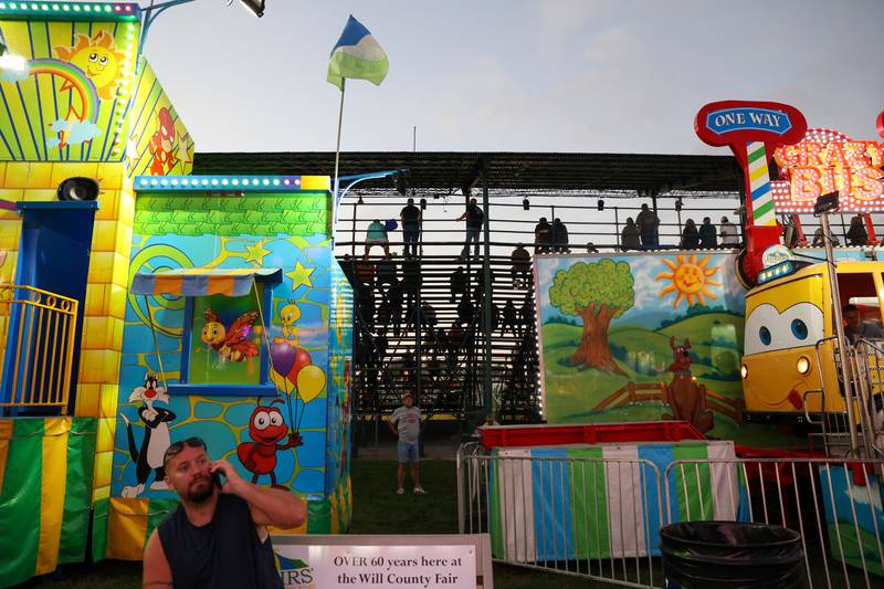 Carnival rides glow as attendees in the grandstand watch the Illinois Tractor Pulling Association Truck and Tractor Pull during the Will County Fair on Aug. 21, 2025.