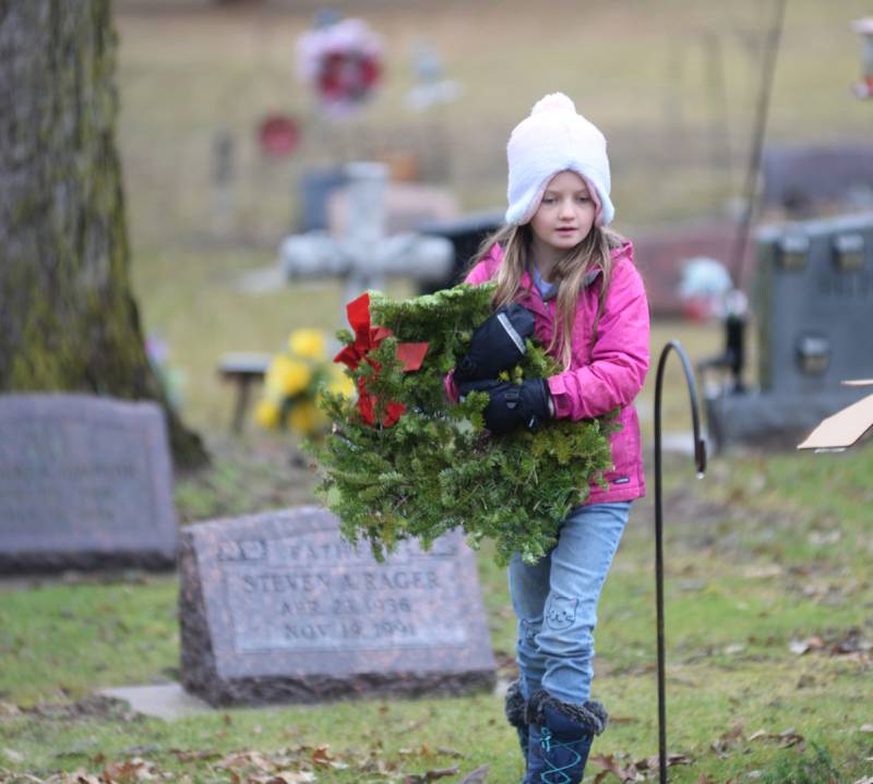 Lana Becker, 7, of Oregon, carries wreath to a veteran's grave at the Wreaths Across America event at Daysville Cemetery. east of Oregon, on Saturday, Dec. 16, 2023. Lana along with her dad Luke and sisters Aven and Remy helped at the event.