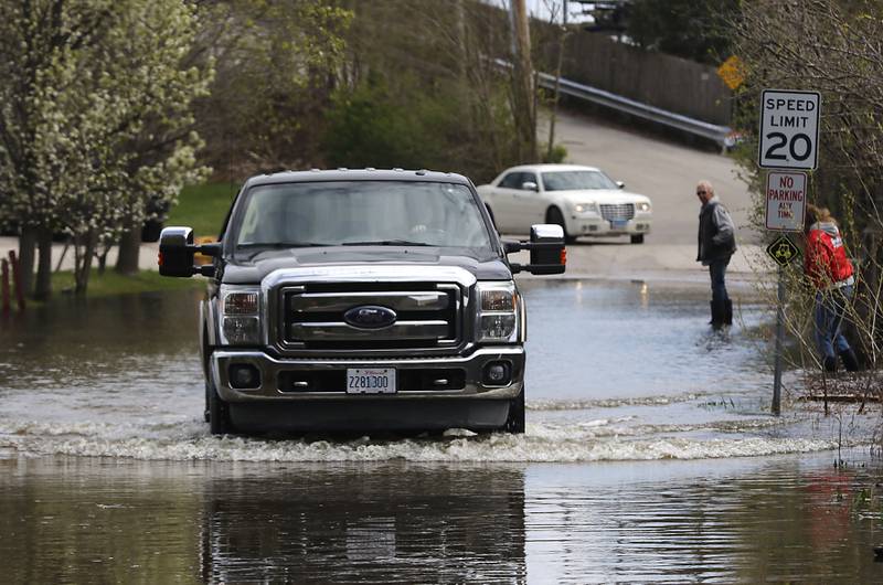 People walk and drive through flood waters on Bald Knob Road near the Bru Crew Bar and Grill  on Sunday, April 19, 2026, in Johnsburg as the Fox River continues to rise.
