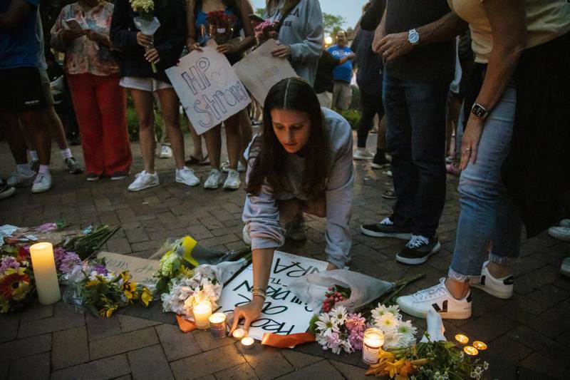 Dozens of mourners gather for a vigil near Central Avenue and St. Johns Avenue in downtown Highland Park, one day after a gunman killed at least seven people and wounded dozens more by firing an AR-15-style rifle from a rooftop onto a crowd attending Highland Park's Fourth of July parade, Tuesday, July 5, 2022 in Highland Park, Ill.. (Ashlee Rezin/Chicago Sun-Times via AP)