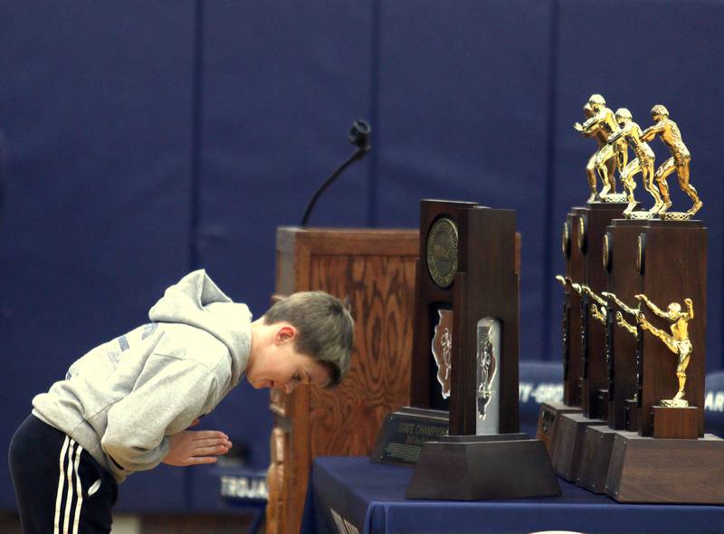 Kane Seaburg, son of Head Coach Brad Seaburg, bows to the 2023 trophy and other assorted hardware during a celebration of the IHSA Class 6A Champion Cary-Grove football team at the high school Sunday. Kane’s brother Peyton QB’d the 2023 team.