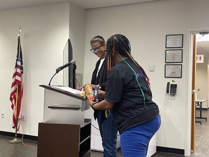 NaKia McAdoo (Left), a principal with Excelleaf Dispensary, is all smiles showing off some of her dispensary's cannabis product packaging at the lectern Tuesday, May 27, 2025, at the DeKalb City Council meeting.