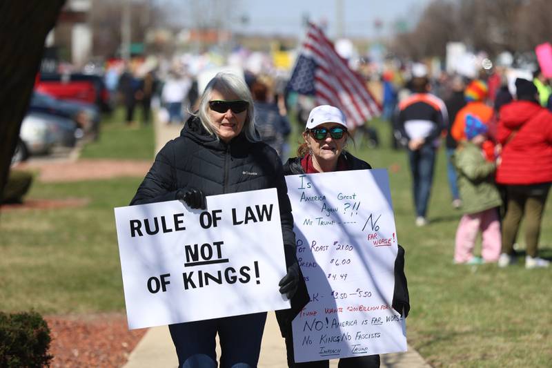 A couple walks along the sidewalk holding signs at the No Kings rally on Saturday, March 28, 2026 in Joliet.