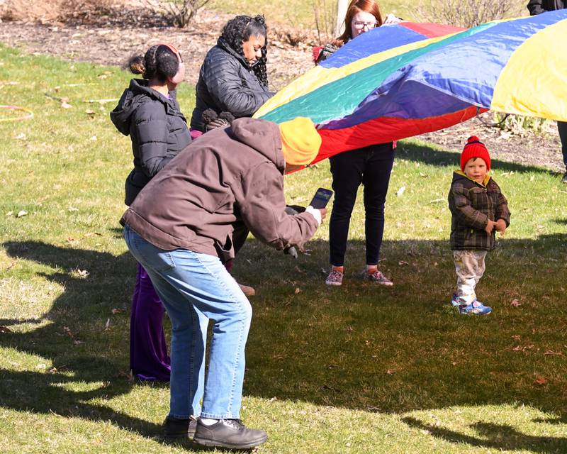 Randy Griffith takes photos of his grandson Colton Griffith, 2, of DeKalb while playing under a parachute before the start of the DeKalb Park District's annual children's egg hunt at Hopkins Park in DeKalb on Saturday, March 23, 2024.