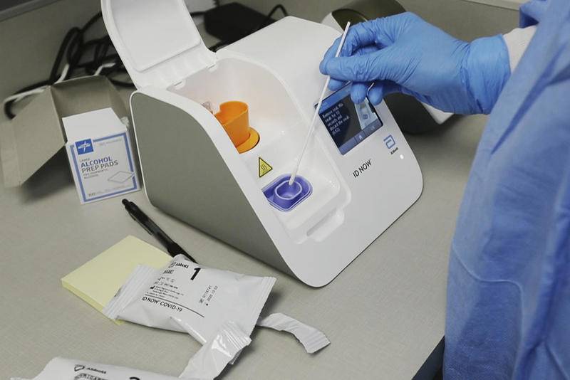 In this image made from video April 10, a lab technician dips a sample into the Abbott Laboratories ID Now testing machine at the Detroit Health Center in Detroit. Federal health officials are warning about potential accuracy problems with the rapid test for COVID-19 used at thousands of hospitals, clinics and testing sites across the U.S., including the White House.