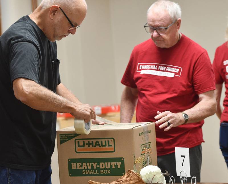 Mark Long and Larry Guenzler of the Evangelical Free Church of Mt. Morris tape up one of the boxes of care packages to be mailed to sailors on the USS Fitzgerald on Thursday, Oct. 16, 2025. Volunteers gathered in the church's basement to assemble the packages.