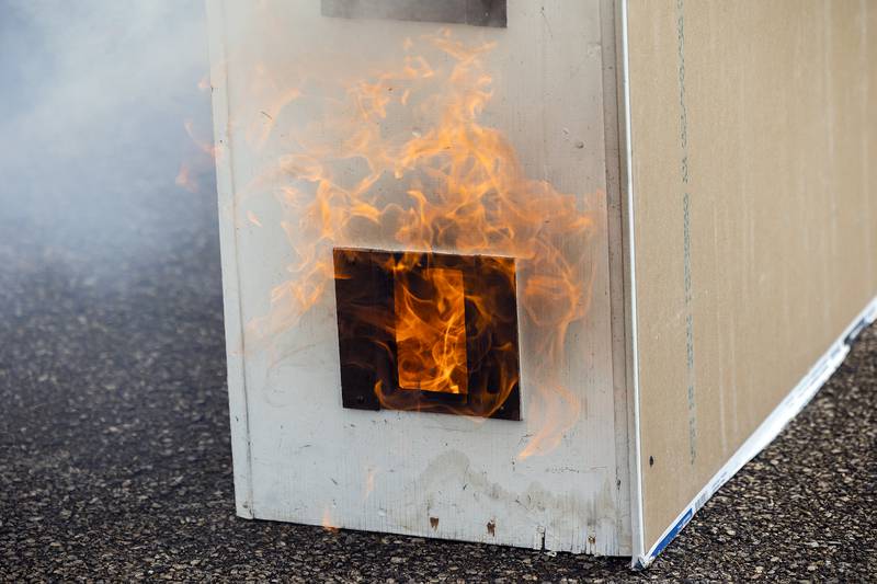 Fire licks out one of the windows of a model home Tuesday, April 22, 2025. Teams of students got together to build the homes and point out where the fire should begin.