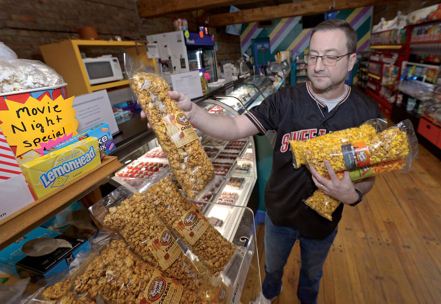 Sweet Tooth owner Kevin Orf adds popcorn to a display rack. The gourmet popcorn is made at the Morris shop.