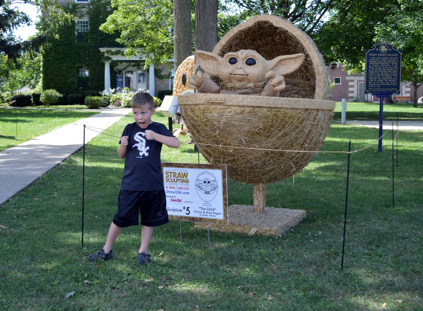 Michael Swanson, 7, of Byron, poses in front of "The Child" in Mt. Morris on Aug. 14, 2021. The straw sculpture of Star Wars' baby Yoda was made by Danica and Mark Rogers of Rochelle as an entry in the U.S. National Straw Sculpting Competition. The competition runs Aug. 13-29 with sculptures displayed on the campus in Mt. Morris. The public can vote for their favorite through Aug. 28.