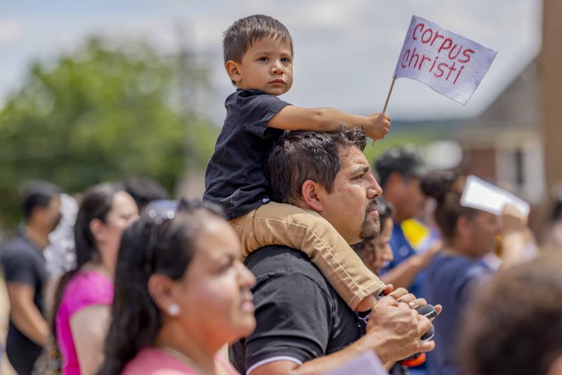Martin Soto sits on his father's shoulders Sunday, June 2, 2024, with a Corpus Christi flag during the three parish procession in La Salle.