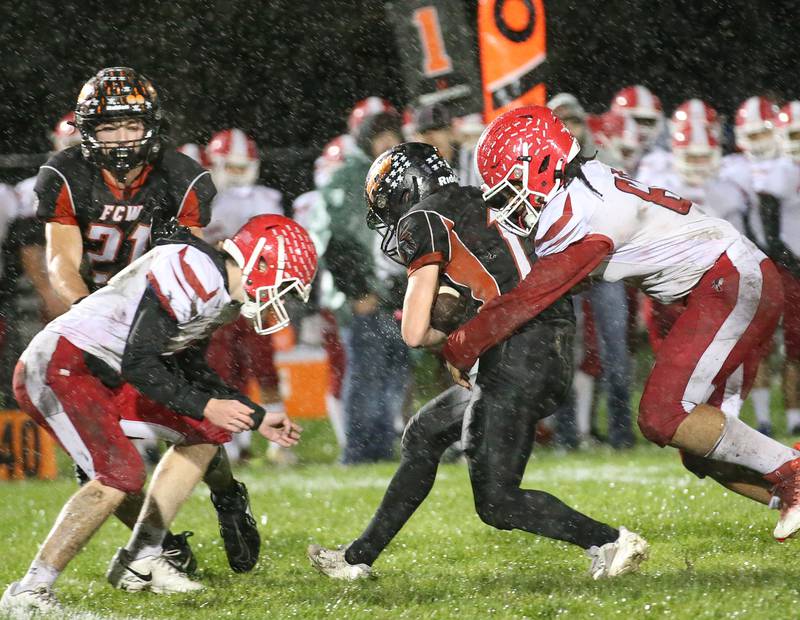 Flanagan-Cornell/Woodland's Payton Quaintance (center) is taken down from behind by South Beloit's Syncere Fane while teammate Toby Hansen pushes South Beloit's Jacob WilHite away from the tackle during the first round of the 8-man football playoffs on Friday, Oct. 27, 2023 in Flanagan.