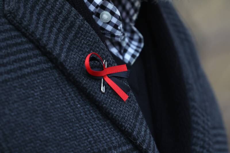 A man wears a red ribbon pin in memory of the victims of the March 5th shooting at a candlelight vigil on Wednesday, March 8th, 2023 in Bolingbrook.