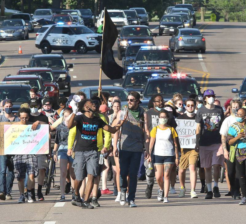 Protesters followed by police blocking traffic behind them march south on Sycamore Road near Clinton Rosette Middle School in DeKalb Tuesday. The group was protesting against police brutality and the recent death of George Floyd.