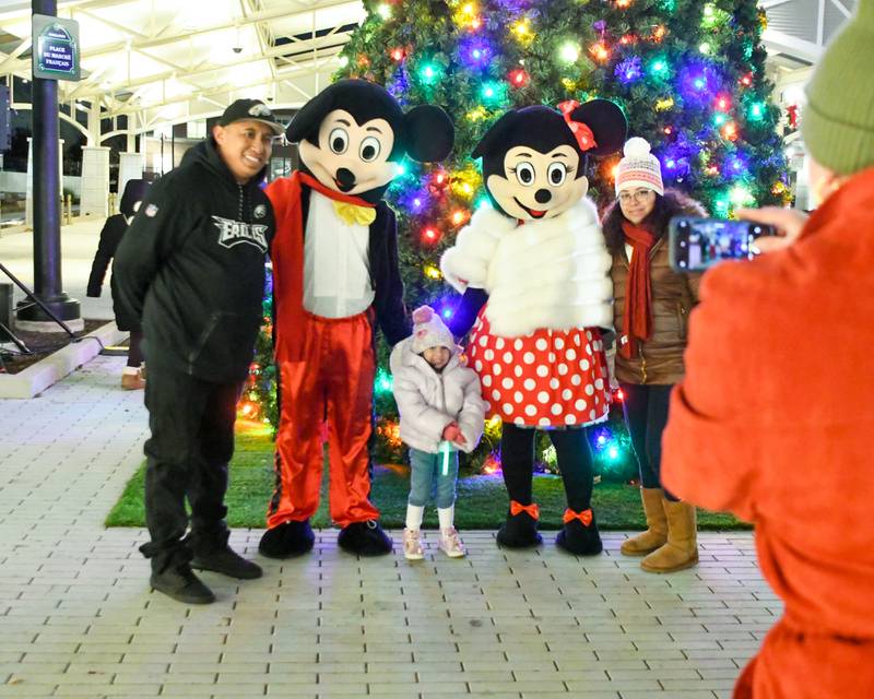 Carole Kohout of Wheaton takes a picture for Mario and his wife Xiomara Mendez along with their daughter Andrea Mendez, 3 years old, of Wheaton along with Micky and Minnie Mouse after Micky and Minnie help with the tree lighting presentation and taking part in the holiday Parade in downtown Wheaton on Friday Nov. 24, 2023.
