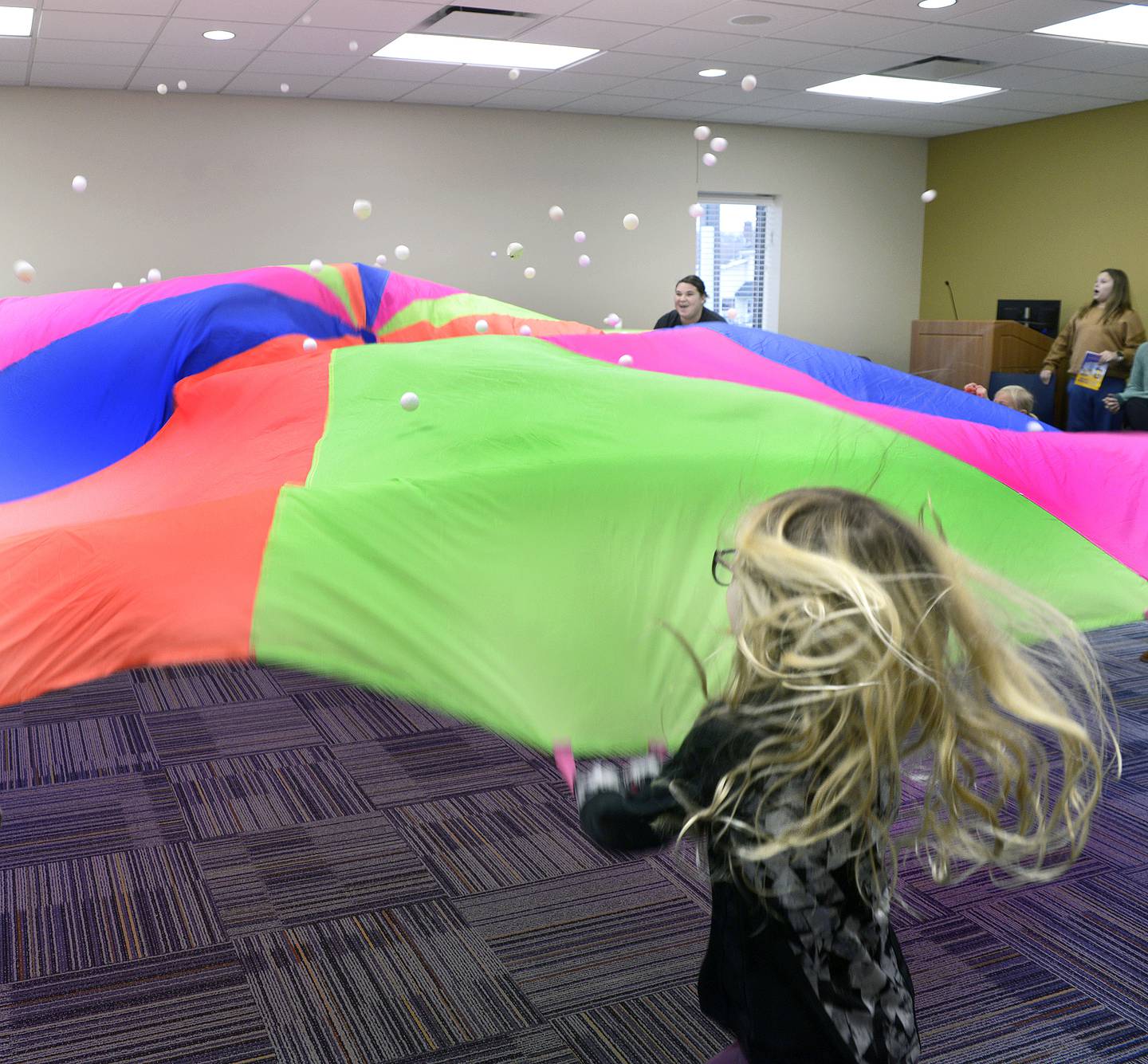 Children toss ping pong balls on a giant parachute Monday at the Reddick Library in Ottawa during the Parachute Play event.