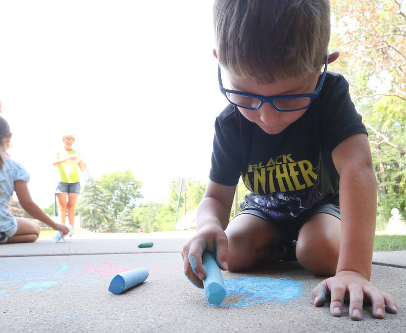 Collin Caputo colors the sidewalk in front of the Peru Public Library during their "Chalk the Walk" event on Tuesday, Aug. 13, 2024.