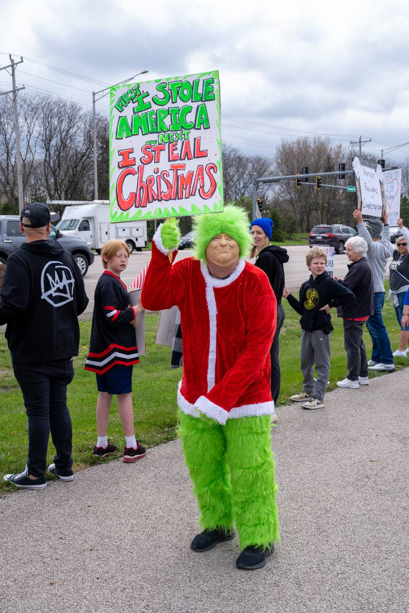 Protester dressed up as The Grinch holds up a protest sign along Randall Road in South Elgin, IL to protest their issues with President Donald J. Trump and his administration and Elon Musk involvement in US government affairs on Saturday April 19, 2025.  Hundreds of protesters participated in the latest Hands Off protest occurring in the Chicagoland area and the rest of the country.