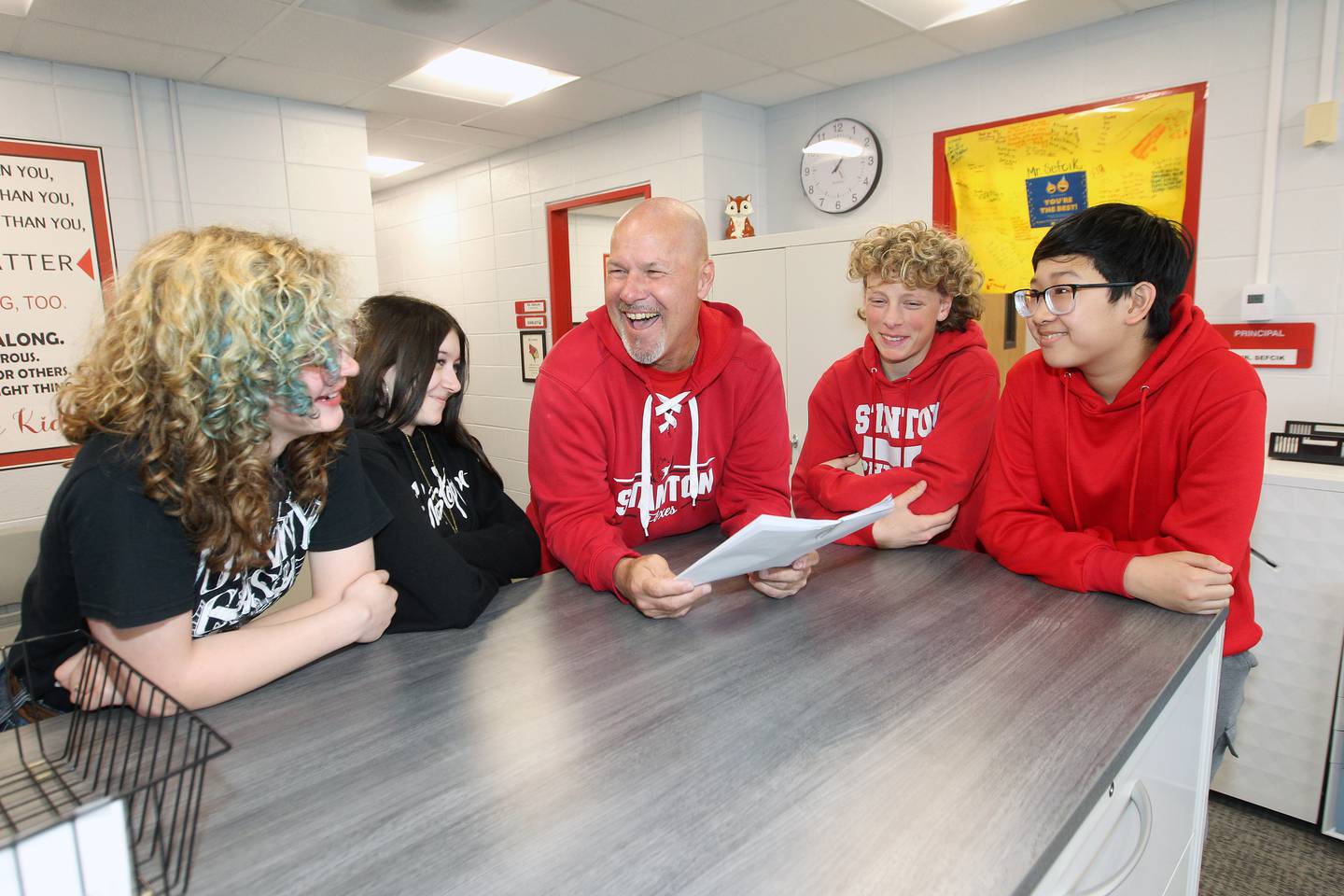 Principal Jeff Sefcik shares a laugh with Stanton Middle School students (left to right) Karianne Lanners, Ava Larson, Mason Gallina, and Michael Van while reading the school’s newsletter, capturing the strong sense of connection and community he’s fostered throughout his years of leadership.
