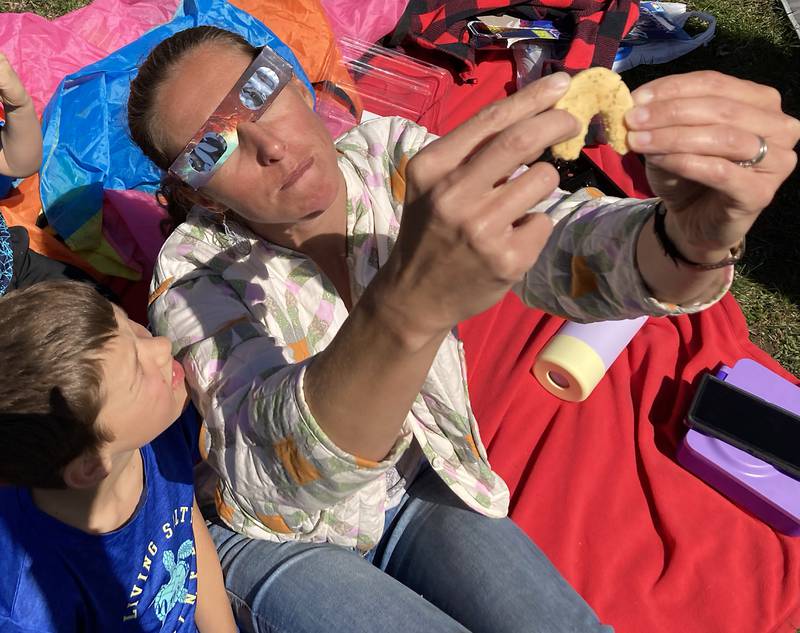 Colleen Bailey of Crystal Lake uses a cookie to show the shape of the eclipse to Caddock, 9, as they watch the partial eclipse Monday, April 8, 2024, at the Crystal Lake Park District's Nature Center.