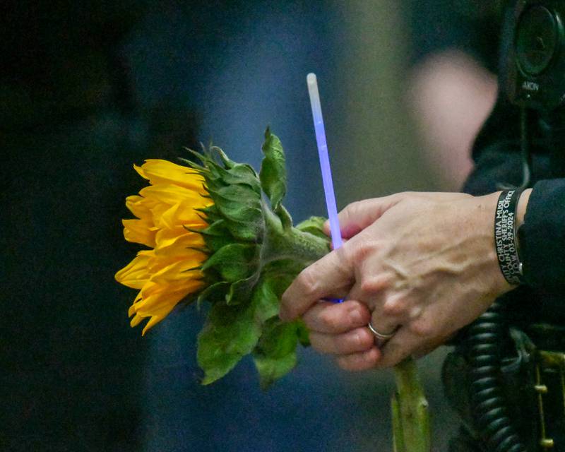 An officer holds a sunflower and a glowstick on Saturday, March 29, 2025, during a memorial vigil to mark one year since the late DeKalb County sheriff's deputy Christina Musil, 35, was killed in the line of duty in a rear-end car crash in Waterman while on patrol on March 28, 2024. The vigil was held at Sycamore High School's field house. Sunflowers were Musil's favorite flower.