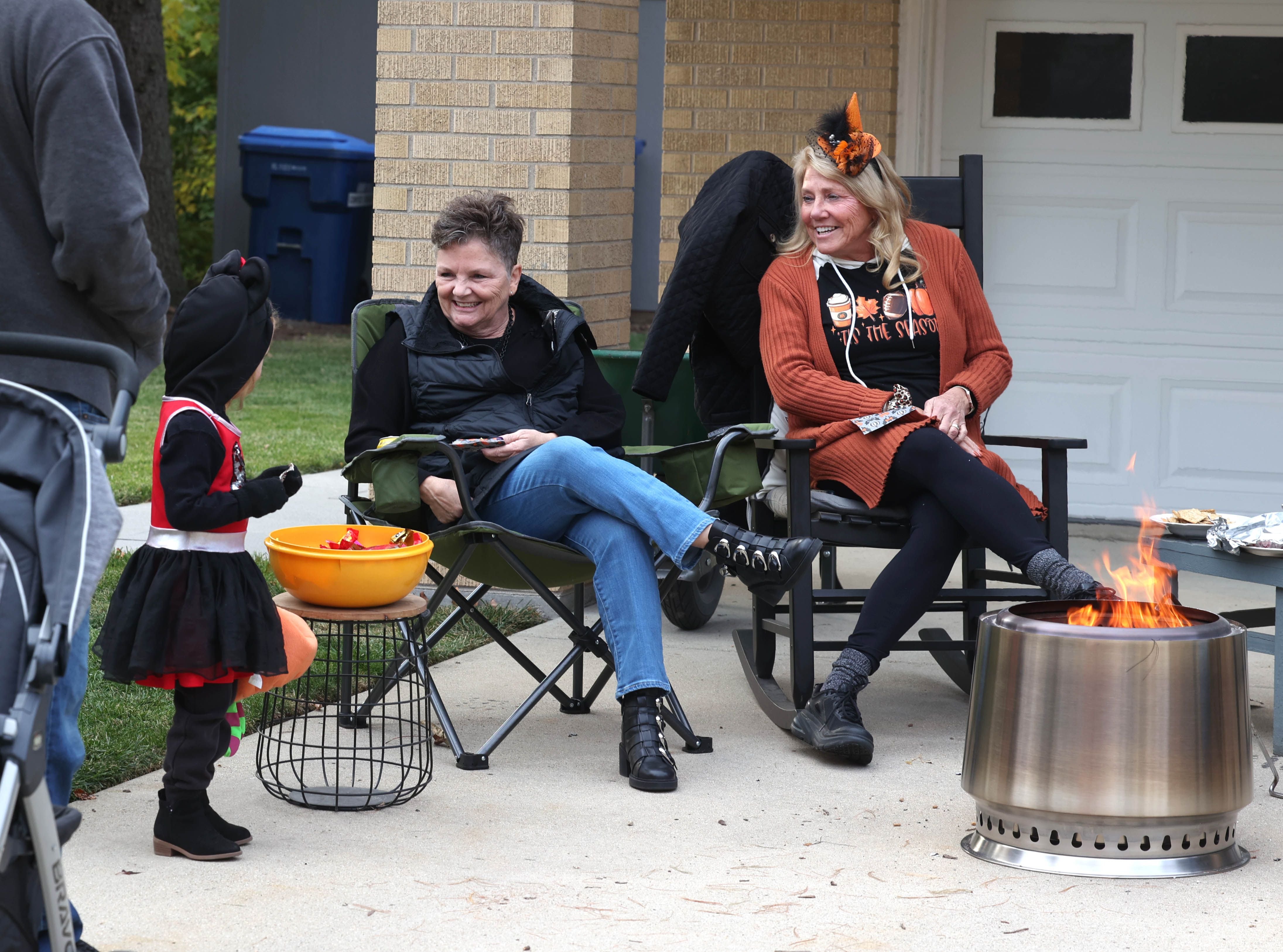 Cathy Ecker (left) and Kim Armour stay warm by the fire as they hand out candy to trick-or-treaters on Halloween, Friday, Oct. 31, 2025, in DeKalb.