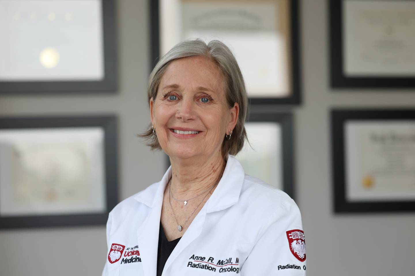 UChicago Medicine radiation oncologist Anne R. McCall, MD stands in front of her numerous degrees and certifications at her office in New Lenox.