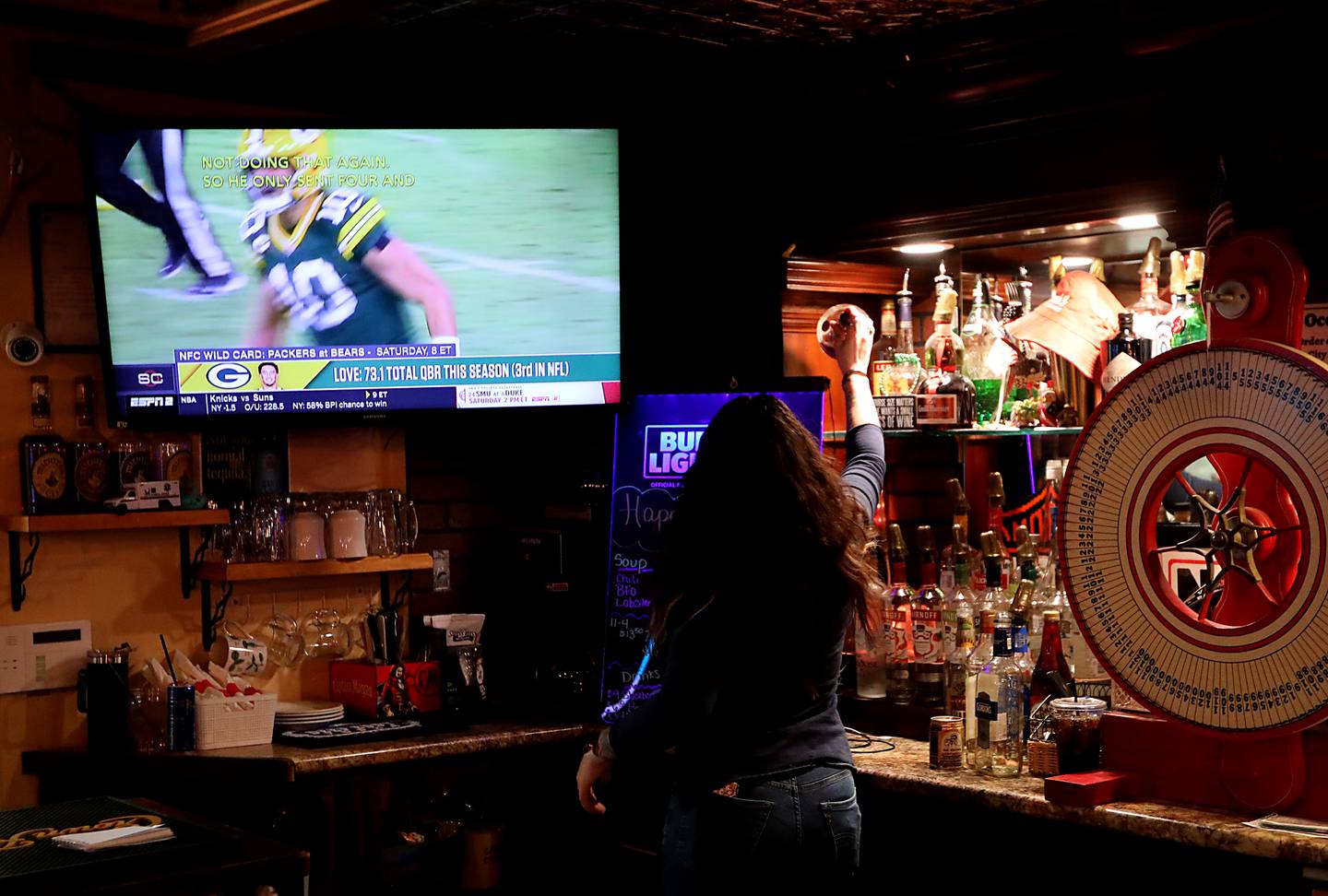 Melissa Jasso grabs a bottle as she makes a drink while Packer highlights play on the television at Herner's Hideaway in Genoa City, Wis., on Friday, Jan 9, 2026. The bar is officially a Green Bay Packer's bar but splits about 50-50 between Packers' fans and Chicago Bears' fans.