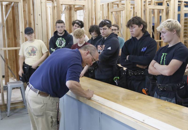 Dan Rohman teaches his construction trades students how to measure out a board to build a stud wall on Tuesday, Aug. 30, 2022, during class at McHenry High School. The students in the class will build the tiny shops that will house incubator retail businesses on McHenry's Riverwalk at Miller Point.