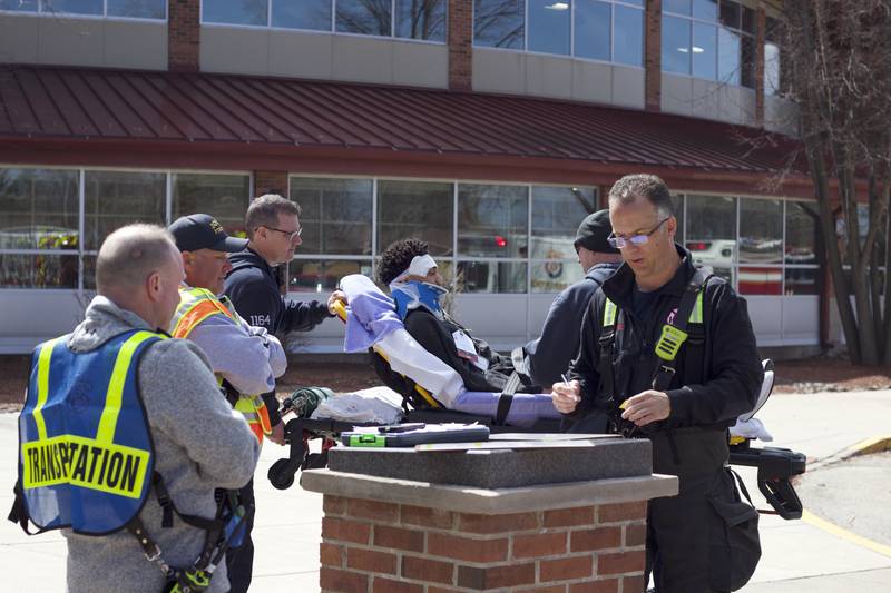 Paramedics taking a student actor to an ambulance outside Joliet West High School on Tuesday, March 25, 2025, as part of a staged emergency drill simulating the aftermath of a gas explosion.