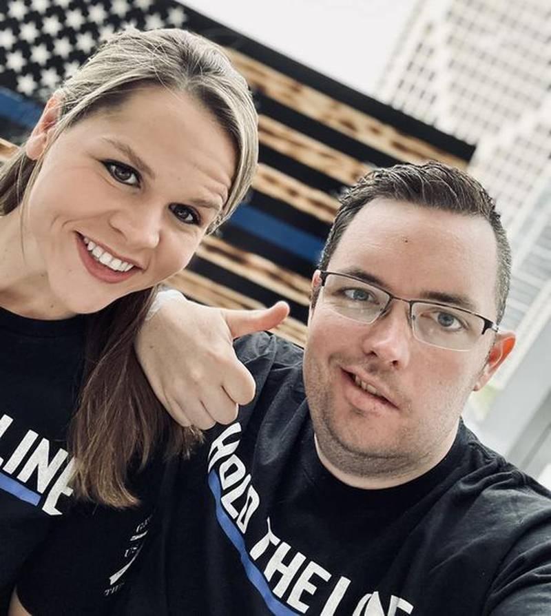 Kara Burroughs (left) and Officer Gazda (right) with the thin blue line flag behind them and AJ giving the thumbs up was taken May 19, 2023, when AJ got home after brain surgery.